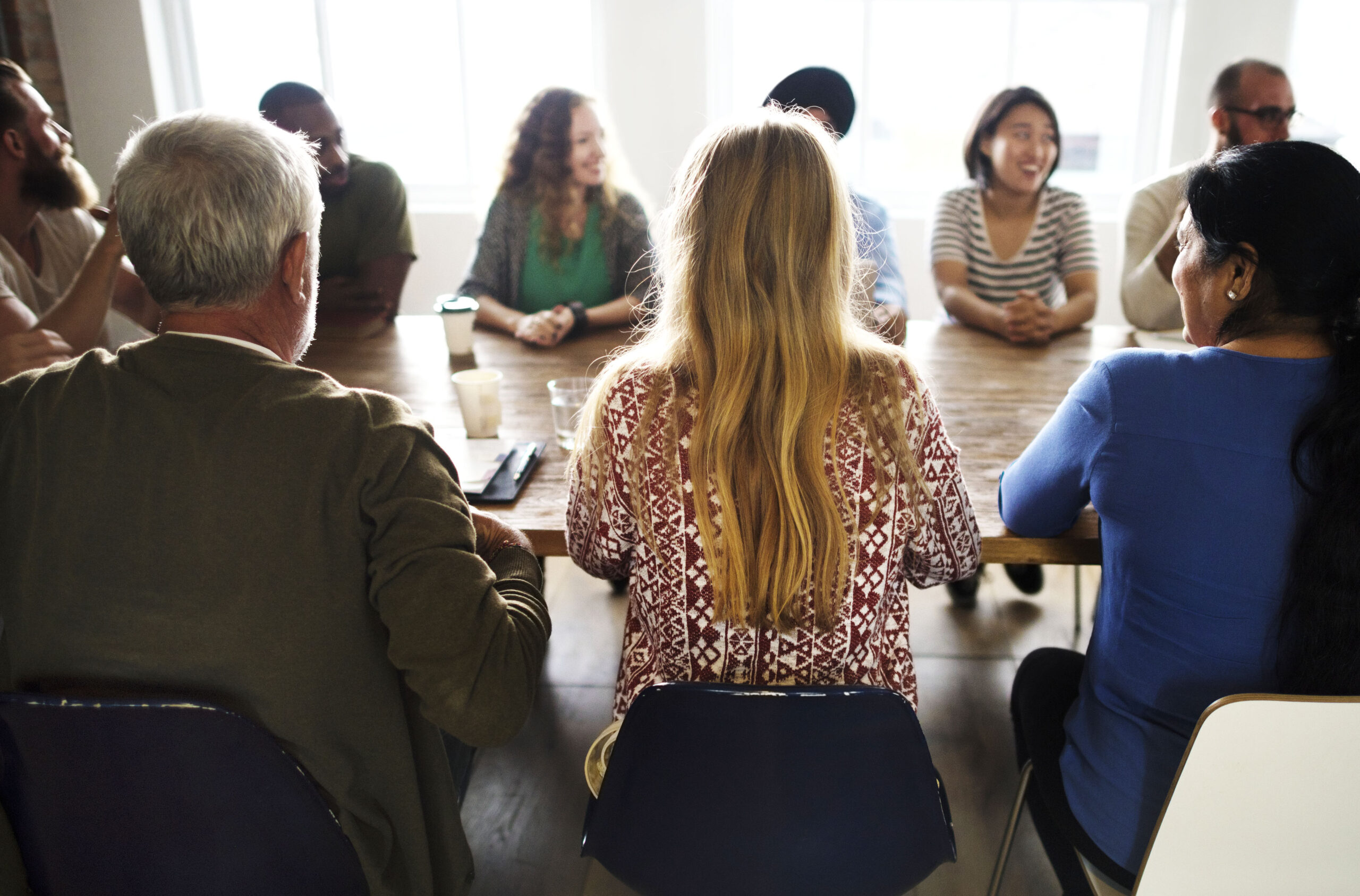 Een diverse groep volwassenen zit rond een tafel tijdens een groepsbijeenkomst en is met elkaar in gesprek