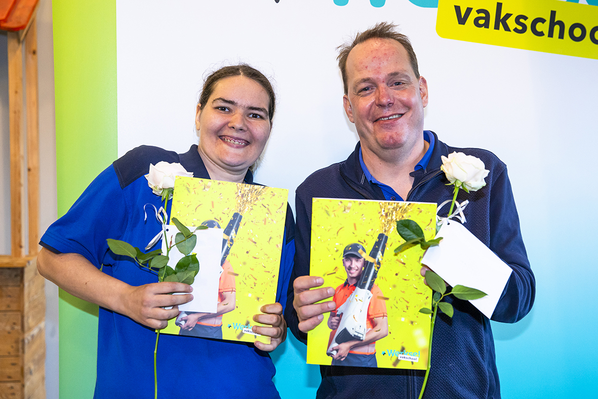 Twee blije cursisten samen op de foto met in hun handen het certificaat en een bloem