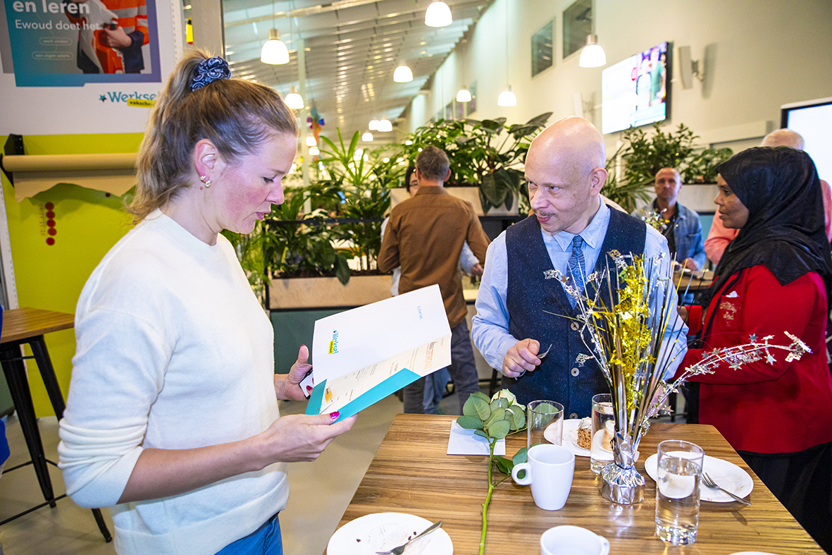 Cursist laat certificaat aan begeleider zien onder het genot van een kopje koffie en een feestelijk taartje