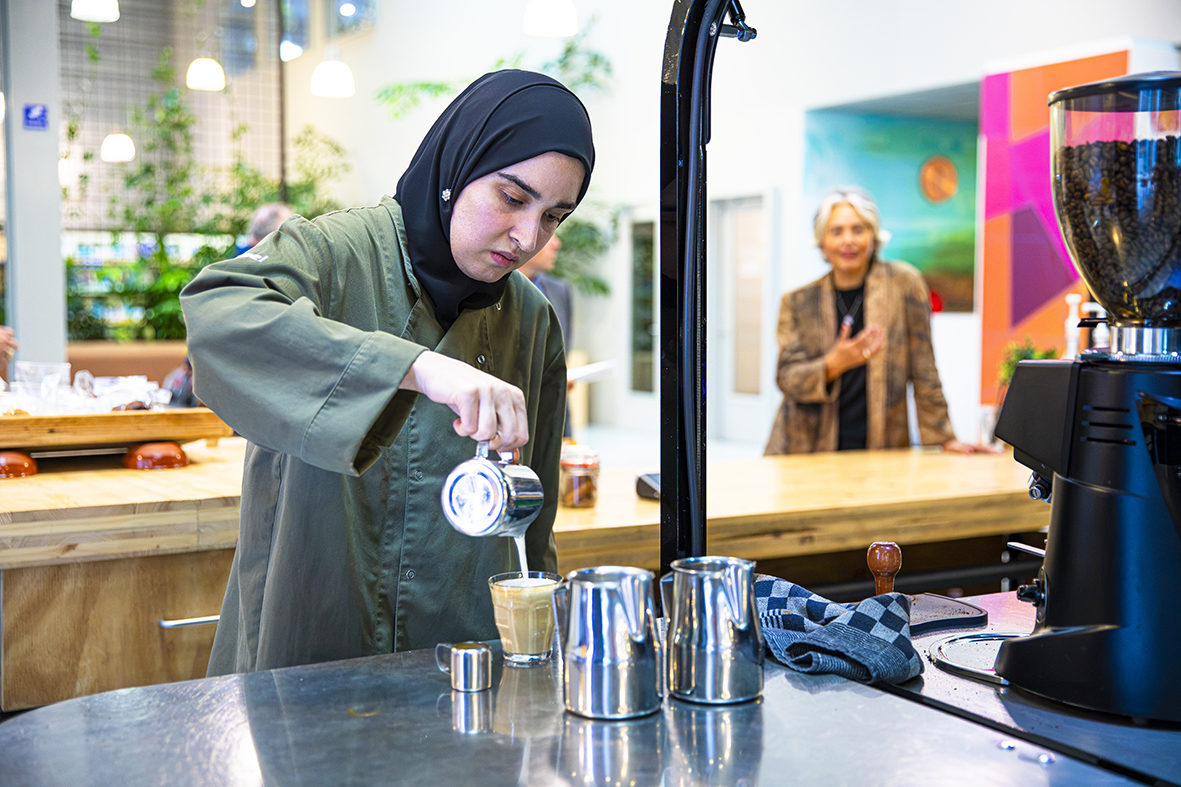 Catering barista medewerker van Werkse! schenkt koffie in voor Hélène Oppatja die op de achtergrond staat