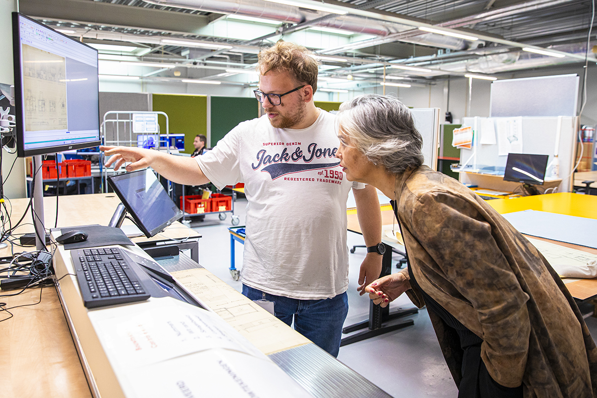 Medewerker legt aan wethouder Hélène Oppatja uit hoe digitaliseren werkt. Beide kijken naar een beeldscherm