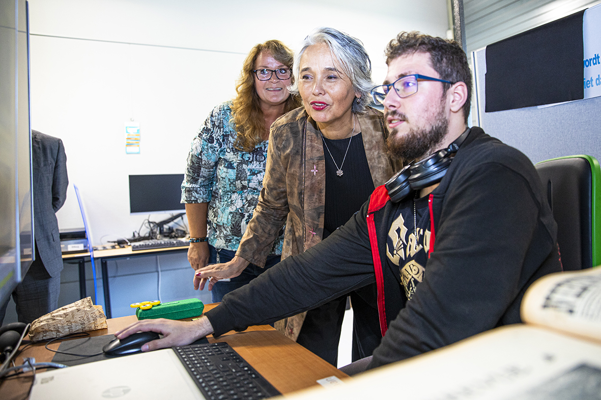 Medewerkers digitaliseren leggen de wethouder uit waarbij allen naar een beeldscherm kijken